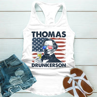 White tank top with graphic design and text, denim shorts, and sandals on a light wooden surface.