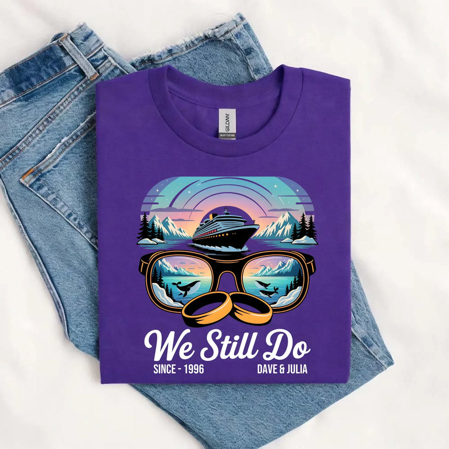 Purple custom tee with cruise ship, sunglasses, wedding rings, and 'We Still Do' text, laid on jeans