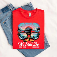 Red custom tee with cruise ship, sunglasses, wedding rings graphic, and anniversary text, folded on jeans.
