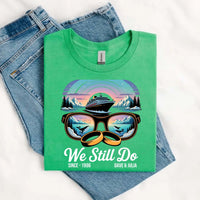Green custom graphic tee with cruise ship, sunglasses, wedding rings, and 'We Still Do' text, styled with blue jeans.