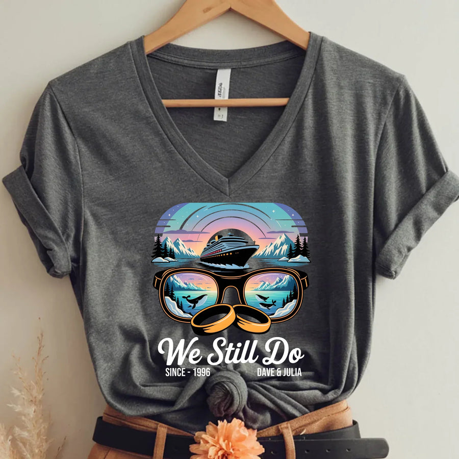 Gray v-neck t-shirt with cruise ship and sunset graphic, sunglasses, and 'We Still Do' text