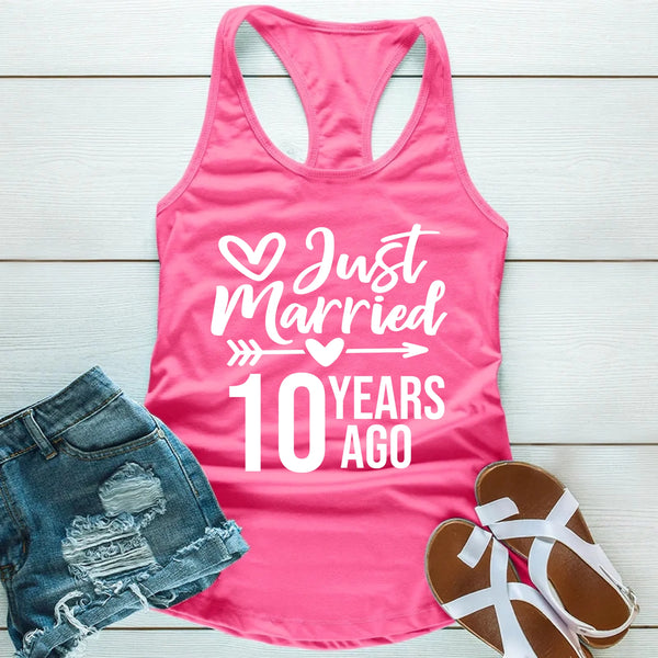 Pink tank top with 'Just Married 10 Years Ago' text, denim shorts, and sandals on a wooden surface.