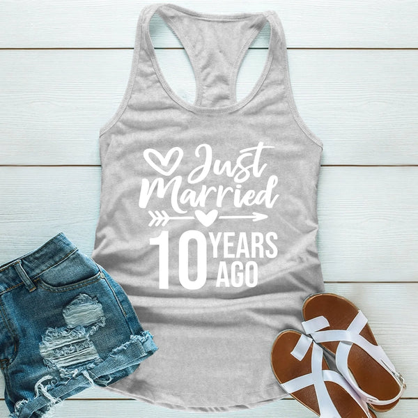 Gray tank top with 'Just Married 10 Years Ago' text, denim shorts, and sandals on a light wooden surface.