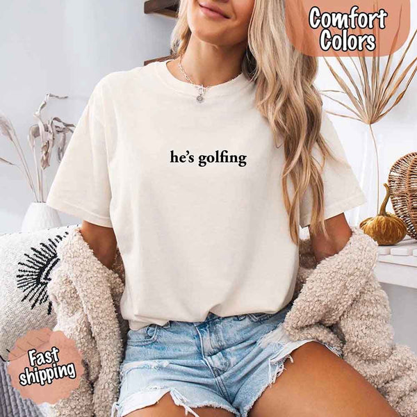 May include a woman wearing an ivory Comfort Colors t-shirt with the phrase 'He’s Golfing' — styled with a relaxed, fun vibe perfect for expressing relationship humor