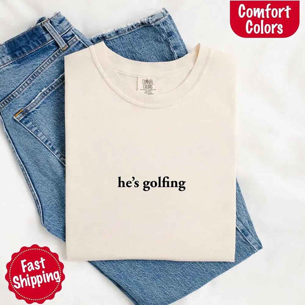 May include an ivory folded Comfort Colors t-shirt with the phrase 'He’s Golfing' — a playful and funny design, great for girlfriends or wives who embrace their man’s golf days