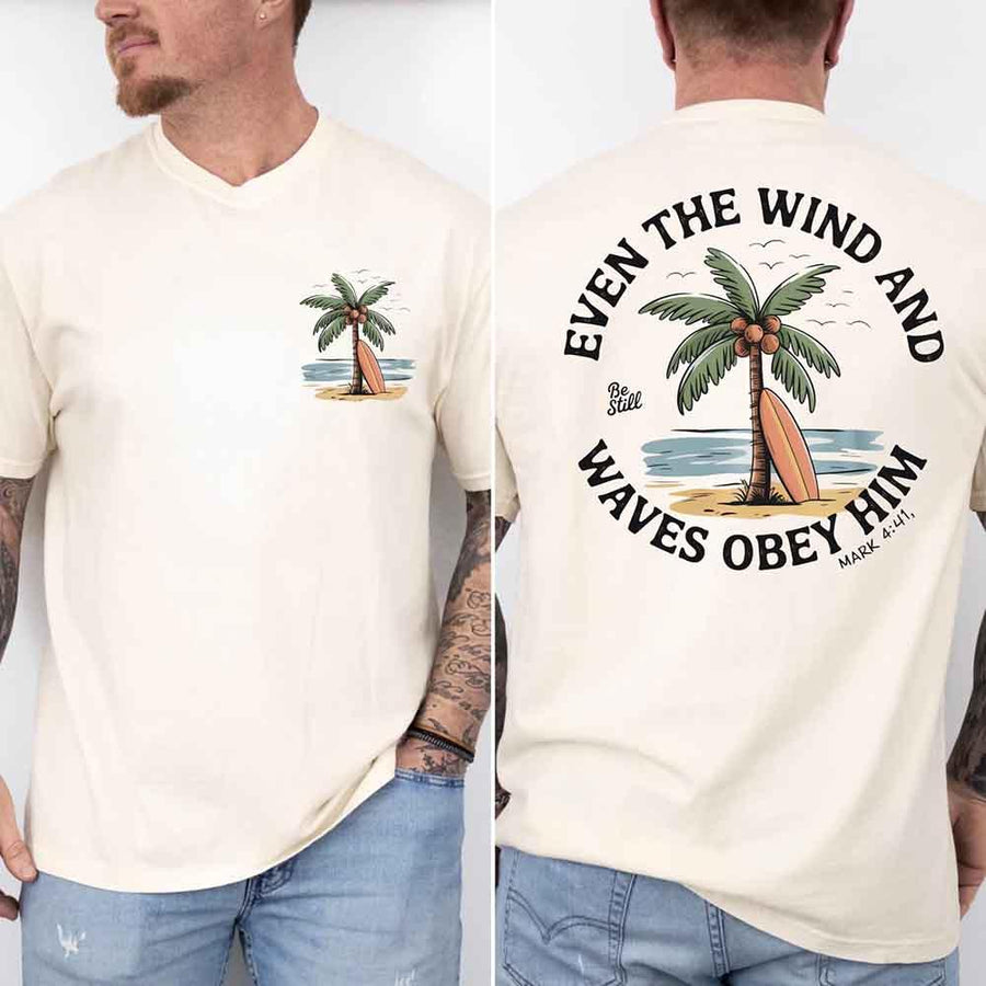 May include a man wearing a cream t-shirt featuring a small front graphic of a palm tree and surfboard, with a larger back design showing the same illustration surrounded by the Bible verse 'Even the Wind and Waves Obey Him – Mark 4:41