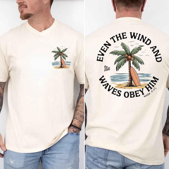 May include a man wearing a cream t-shirt featuring a small front graphic of a palm tree and surfboard, with a larger back design showing the same illustration surrounded by the Bible verse 'Even the Wind and Waves Obey Him – Mark 4:41