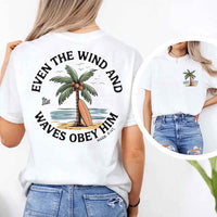 May include a woman wearing a white t-shirt with a small front graphic and a large back design of a palm tree and surfboard by the beach, surrounded by the words 'Even the Wind and Waves Obey Him – Mark 4:41' in a circular layout, inspired by a Christian Bible verse