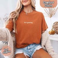 May include a woman wearing a  yam pastel Comfort Colors T-shirt with the phrase “he’s grilling” printed in black text, styled casually for a fun summer look.