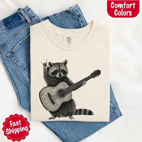 ivory comfort colors T-shirt with raccoon playing guitar design on jeans, with 'Comfort Colors' branding.