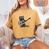 May include a woman wearing a mustard Comfort Colors T-shirt featuring a graphic of a raccoon playing a guitar, styled for a quirky and fun animal lover look.