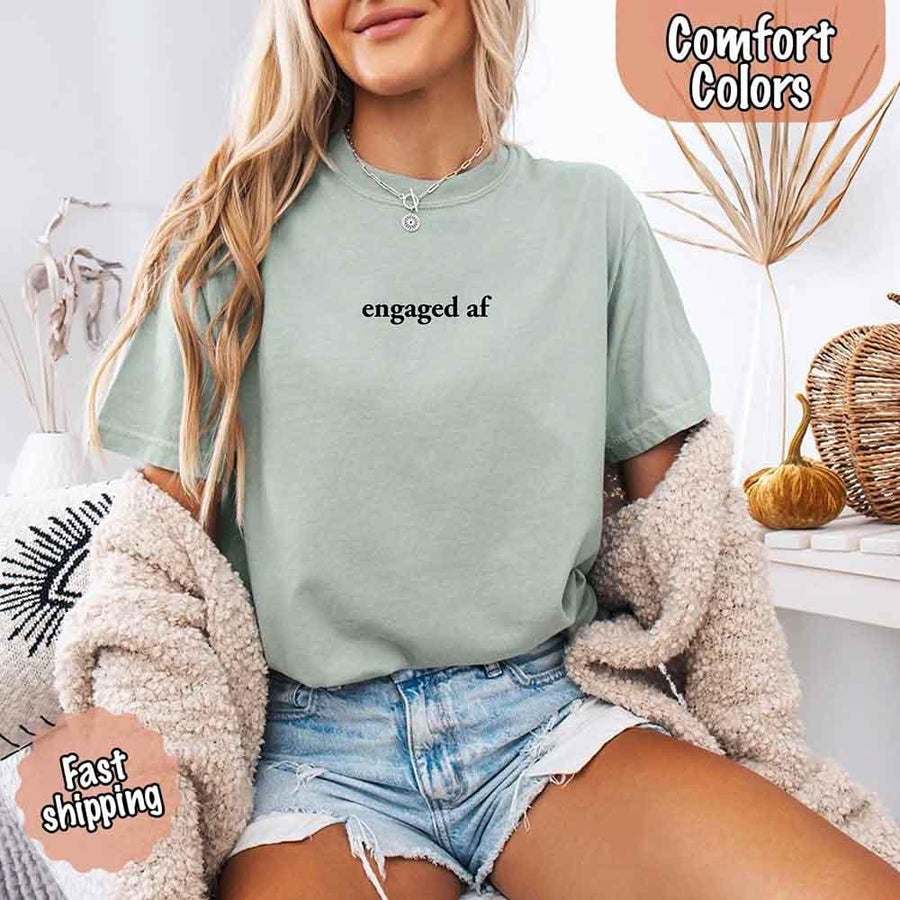 May include a woman wearing a bay Comfort Colors T-shirt with the phrase “engaged AF” in bold black text, styled as a fun and casual engagement outfit.