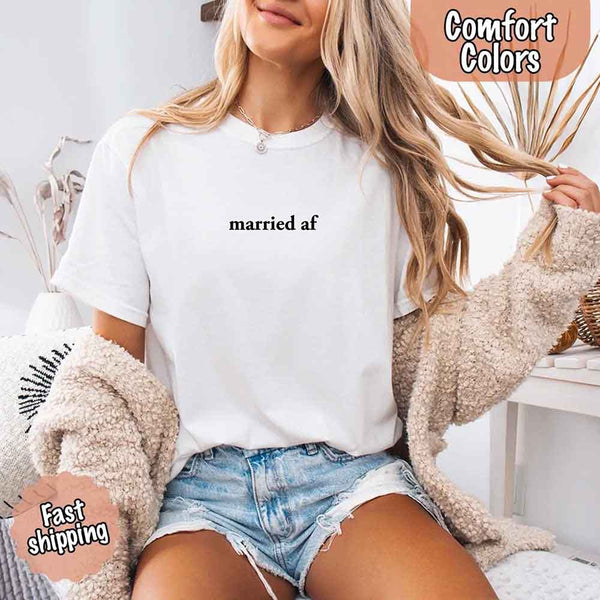 May include a woman wearing a white Comfort Colors T-shirt with the phrase “married AF” in bold black text, styled casually as a fun just-married outfit.