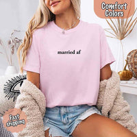 May include a woman wearing a blossom Comfort Colors T-shirt with the phrase “married AF” in bold black text, styled casually as a fun just-married outfit.