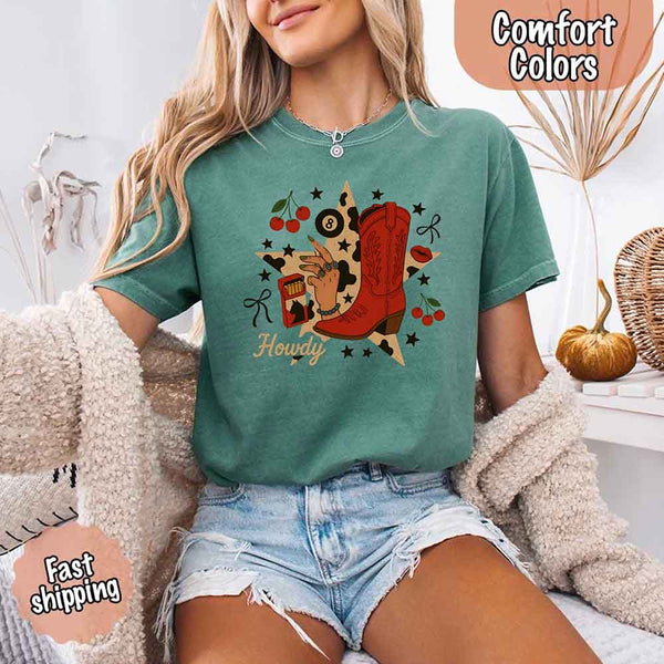 May include a woman wearing a light green Comfort Colors T-shirt featuring the word “howdy” with a colorful star collage design, styled in a fun western or cowgirl-inspired look.