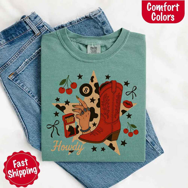 May include a folded light green Comfort Colors T-shirt with a vibrant “howdy” and star collage graphic, laid over denim jeans for a bold western aesthetic.