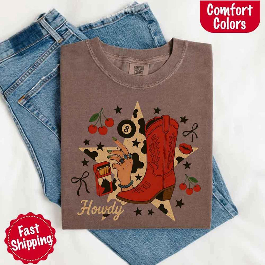 May include a folded espresso Comfort Colors T-shirt featuring the word “howdy” with a colorful star collage design, styled in a fun western or cowgirl-inspired look.