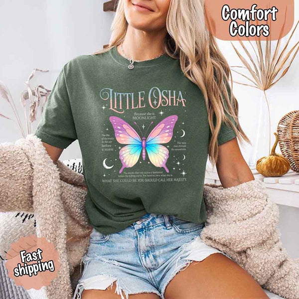 May include a woman wearing a Moss Comfort Colors T-shirt featuring a delicate butterfly graphic inspired by Little Osha from Quicksilver, styled casually with denim for a soft and whimsical look.