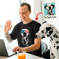 Man wearing a black t-shirt with a dalmatian design, sitting at a desk with a dog looking at the camera.