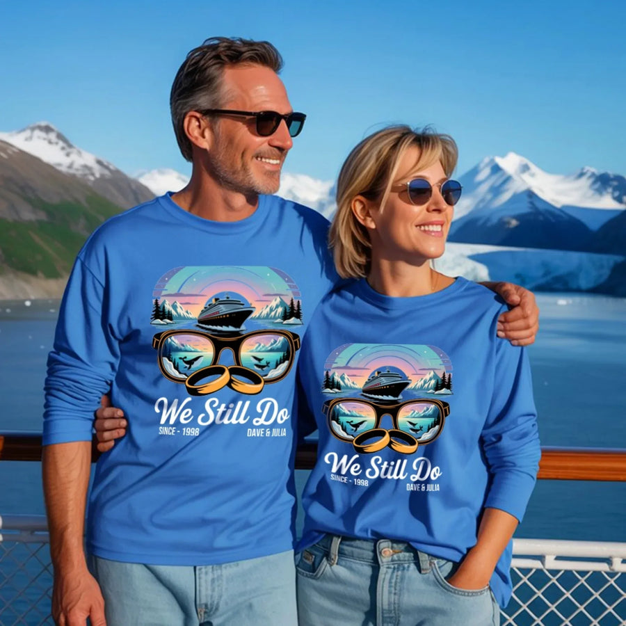 Smiling couple in matching blue custom tees with cruise and nature graphic, We Still Do text, on scenic mountain deck