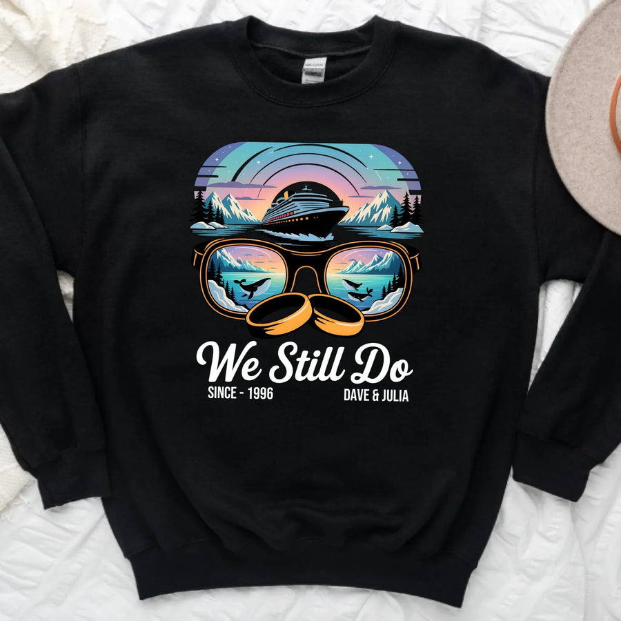 Black sweatshirt featuring retro sunglasses with cruise ship, whales, and mountain sunset graphic, plus text 'We Still Do'.