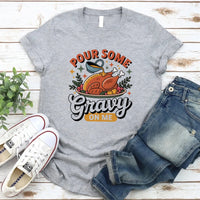 Gray t-shirt with a graphic design and text, paired with jeans and sneakers on a wooden surface.