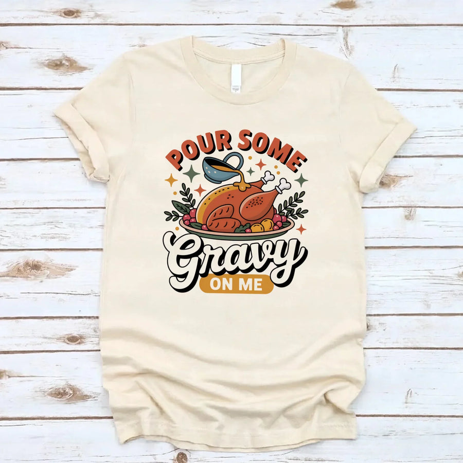 Beige t-shirt with a graphic design and text 'Pour Some Gravy On Me' on a wooden surface