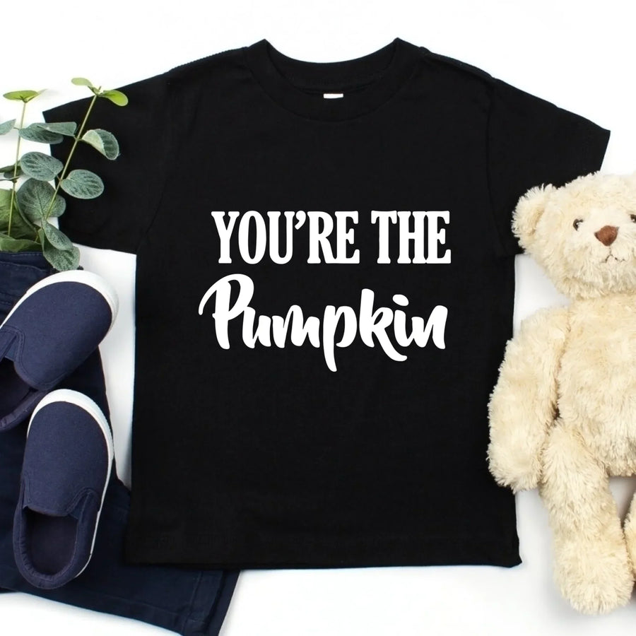 Black t-shirt with 'YOU'RE THE Pumpkin' text, navy shoes, and beige teddy bear on a white background