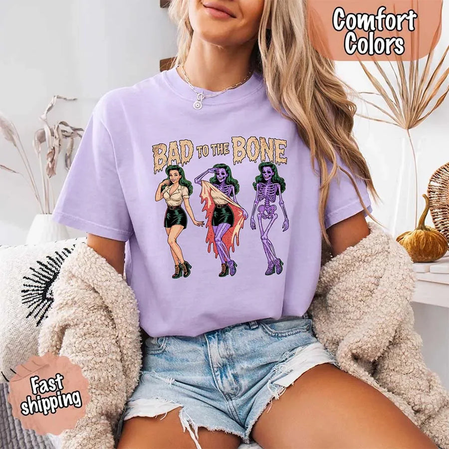 May include Bad to the Bone graphic with retro pin-up girl transforming into purple skeleton artwork – vintage Halloween shirt.