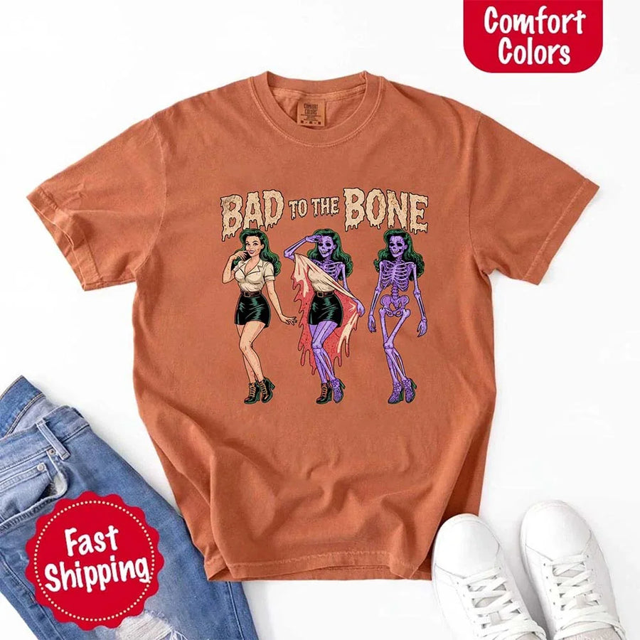 May include Bad to the Bone graphic with retro pin-up girl transforming into purple skeleton artwork – vintage Halloween shirt.