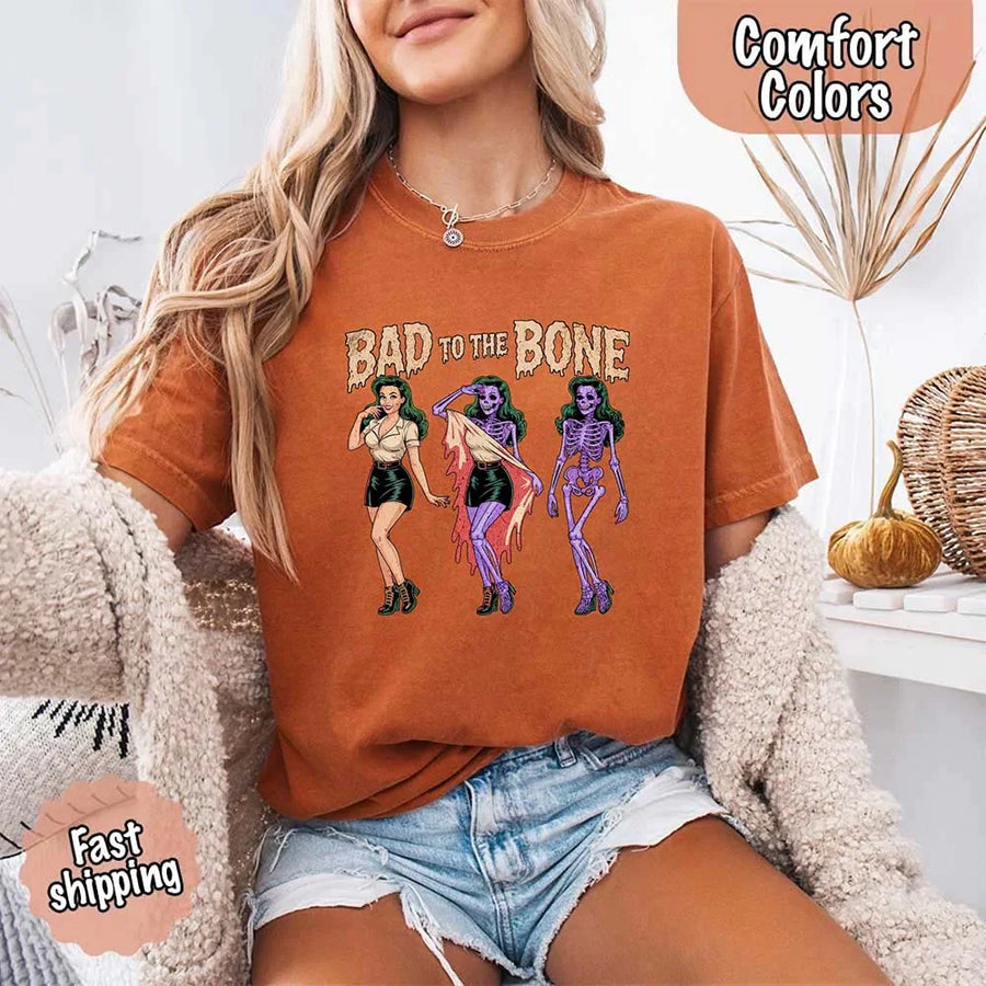 May include Bad to the Bone graphic with retro pin-up girl transforming into purple skeleton artwork – vintage Halloween shirt.