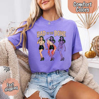 May include Bad to the Bone graphic with retro pin-up girl transforming into purple skeleton artwork – vintage Halloween shirt.