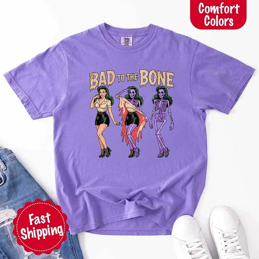 May include Bad to the Bone graphic with retro pin-up girl transforming into purple skeleton artwork – vintage Halloween shirt.