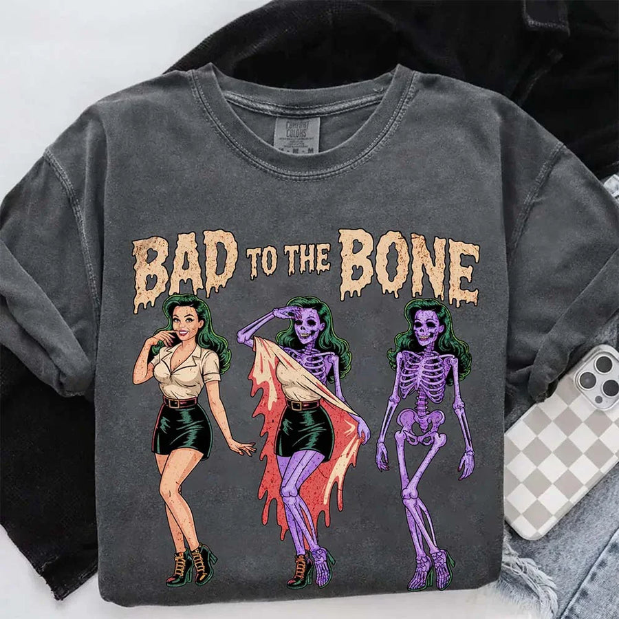 May include Bad to the Bone graphic with retro pin-up girl transforming into purple skeleton artwork – vintage Halloween shirt.