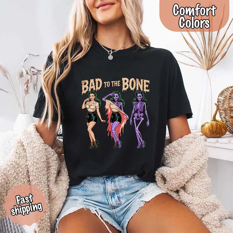 May include Bad to the Bone graphic with retro pin-up girl transforming into purple skeleton artwork – vintage Halloween shirt.