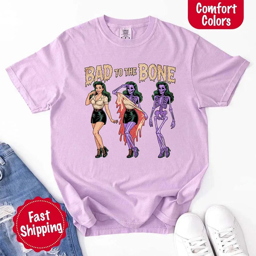 May include Bad to the Bone graphic with retro pin-up girl transforming into purple skeleton artwork – vintage Halloween shirt.