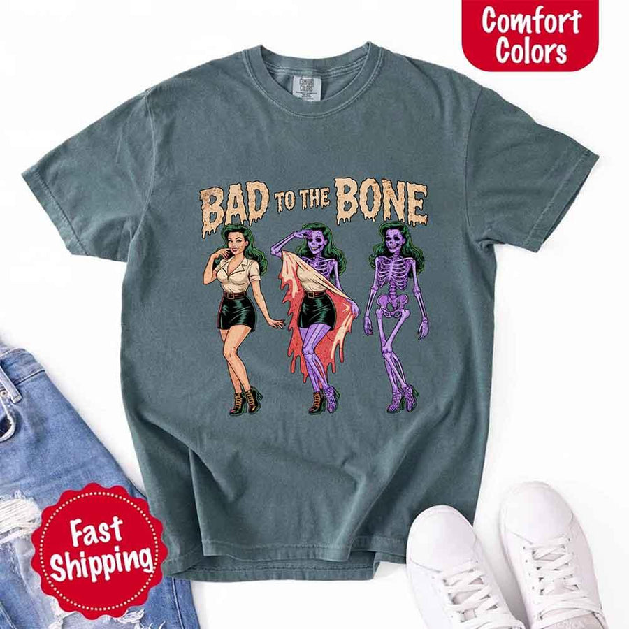 May include Bad to the Bone graphic with retro pin-up girl transforming into purple skeleton artwork – vintage Halloween shirt.