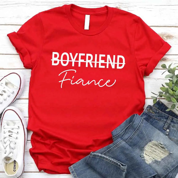 Black t-shirt with 'BOYFRIEND Fiançée' text, paired with jeans and sneakers on a wooden surface.