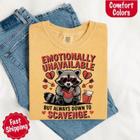 May include a red and black raccoon illustration wearing red sunglasses with the phrase “Emotionally Unavailable,” printed on a Comfort Colors tee for a bold, edgy vibe.