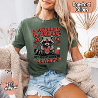 May include a red and black raccoon illustration wearing red sunglasses with the phrase “Emotionally Unavailable,” printed on a Comfort Colors tee for a bold, edgy vibe.