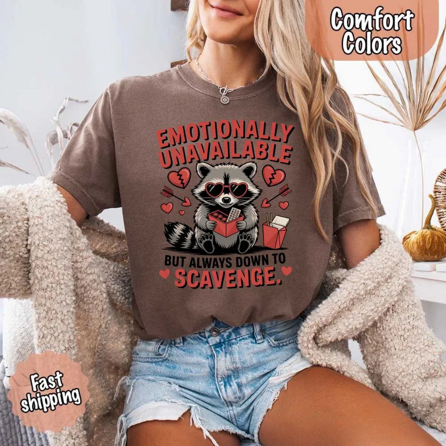 May include a red and black raccoon illustration wearing red sunglasses with the phrase “Emotionally Unavailable,” printed on a Comfort Colors tee for a bold, edgy vibe.