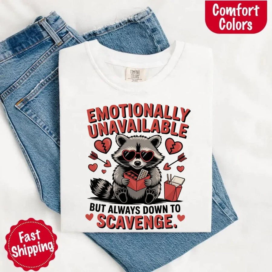 May include a red and black raccoon illustration wearing red sunglasses with the phrase “Emotionally Unavailable,” printed on a Comfort Colors tee for a bold, edgy vibe.
