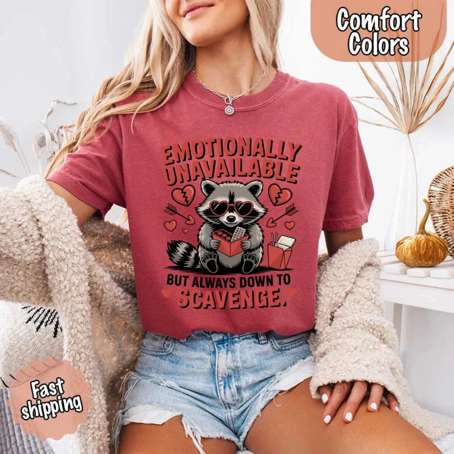 May include a red and black raccoon illustration wearing red sunglasses with the phrase “Emotionally Unavailable,” printed on a Comfort Colors tee for a bold, edgy vibe.