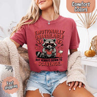 May include a red and black raccoon illustration wearing red sunglasses with the phrase “Emotionally Unavailable,” printed on a Comfort Colors tee for a bold, edgy vibe.