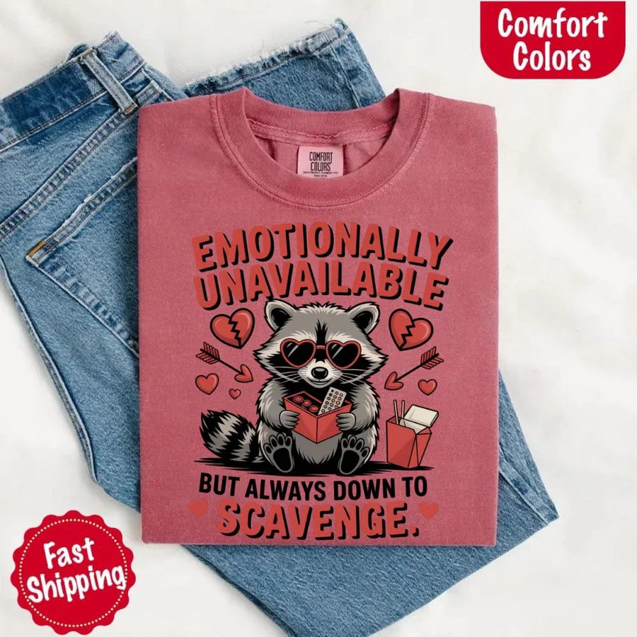 May include a red and black raccoon illustration wearing red sunglasses with the phrase “Emotionally Unavailable,” printed on a Comfort Colors tee for a bold, edgy vibe.