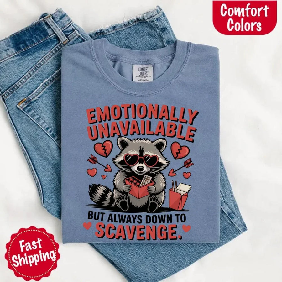 May include a red and black raccoon illustration wearing red sunglasses with the phrase “Emotionally Unavailable,” printed on a Comfort Colors tee for a bold, edgy vibe.