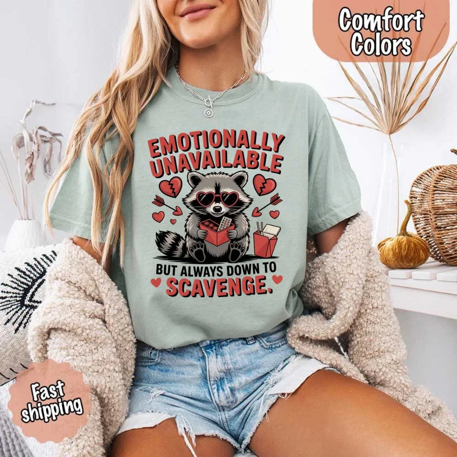 May include a red and black raccoon illustration wearing red sunglasses with the phrase “Emotionally Unavailable,” printed on a Comfort Colors tee for a bold, edgy vibe.