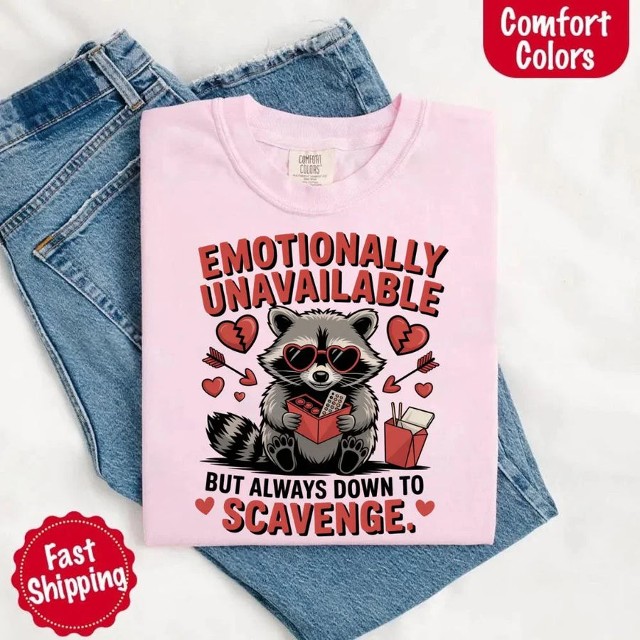 May include a red and black raccoon illustration wearing red sunglasses with the phrase “Emotionally Unavailable,” printed on a Comfort Colors tee for a bold, edgy vibe.