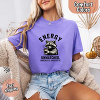 May include a black and white raccoon illustration with a tired, unbothered expression, holding a coffee cup, and bold text that reads “ENERGY UNMATCHED. UNMEDICATED. UNAPOLOGETIC.” conveying raw, unapologetic humor and mood.
