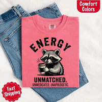 May include a black and white raccoon illustration with a tired, unbothered expression, holding a coffee cup, and bold text that reads “ENERGY UNMATCHED. UNMEDICATED. UNAPOLOGETIC.” conveying raw, unapologetic humor and mood.